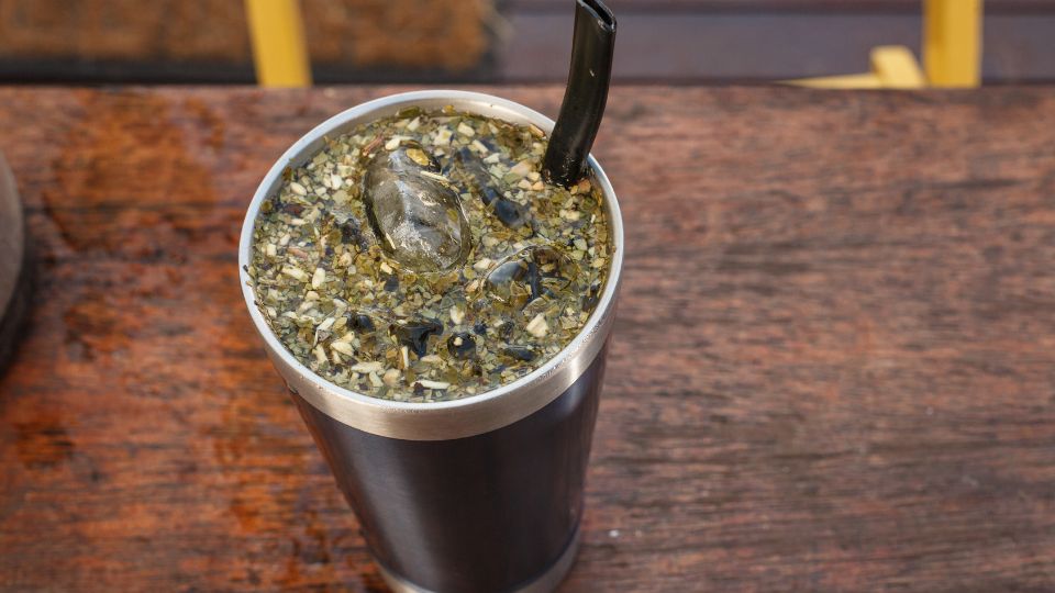 Traditional Paraguayan tereré in a stainless steel guampa with ice and a bombilla straw, sitting on a rustic wooden table.