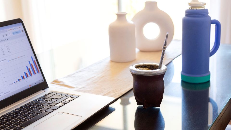 Laptop with productivity chart, yerba mate gourd, and thermos on a modern desk setup