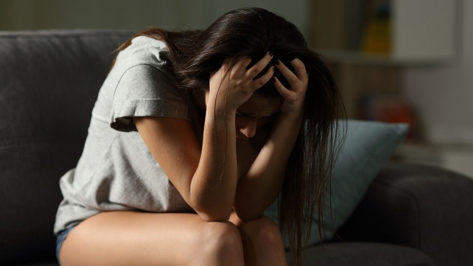 Woman sitting on a couch with her head in her hands, showing signs of anxiety or stress